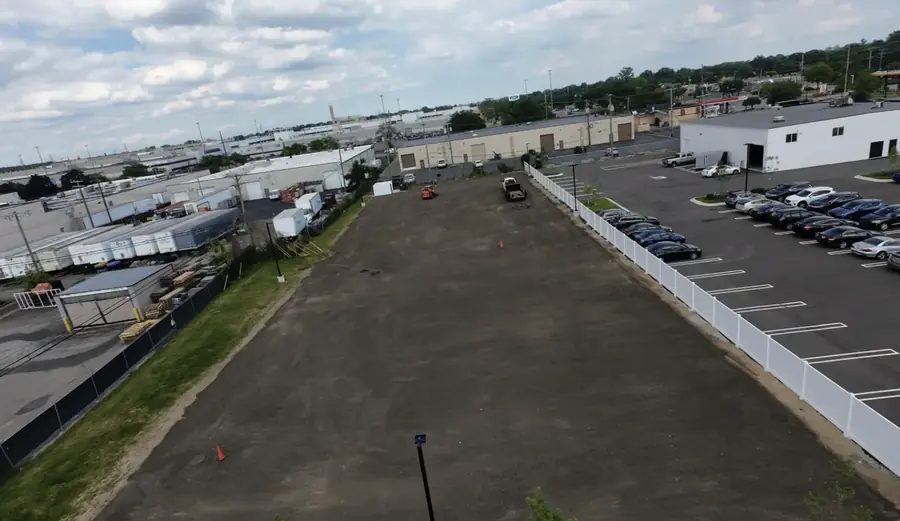 Aerial view of a long storage lot resurfaced with asphalt millings beside a fenced parking area