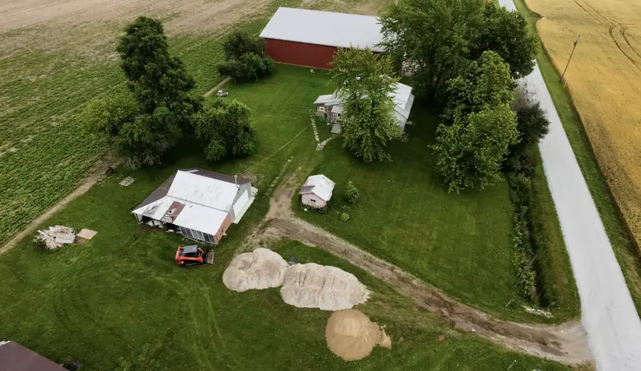 Aerial view of a farmstead with a new gravel drive and stone piles near the outbuildings