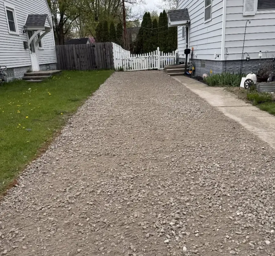 Gravel drive running beside a white house to the back yard