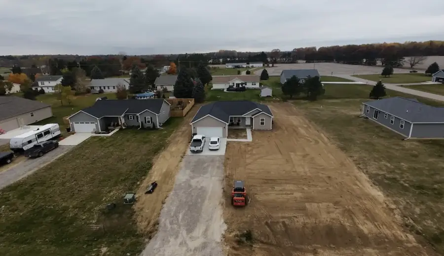 Aerial view of a new-build lot graded beside a gravel drive in a subdivision